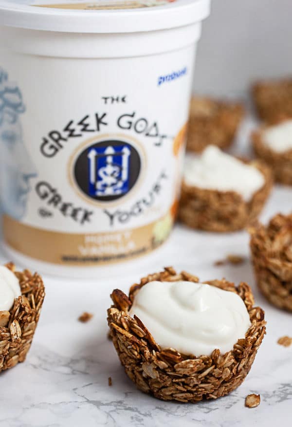 Baked oatmeal cups with yogurt and tub of Greek Gods yogurt on white surface.