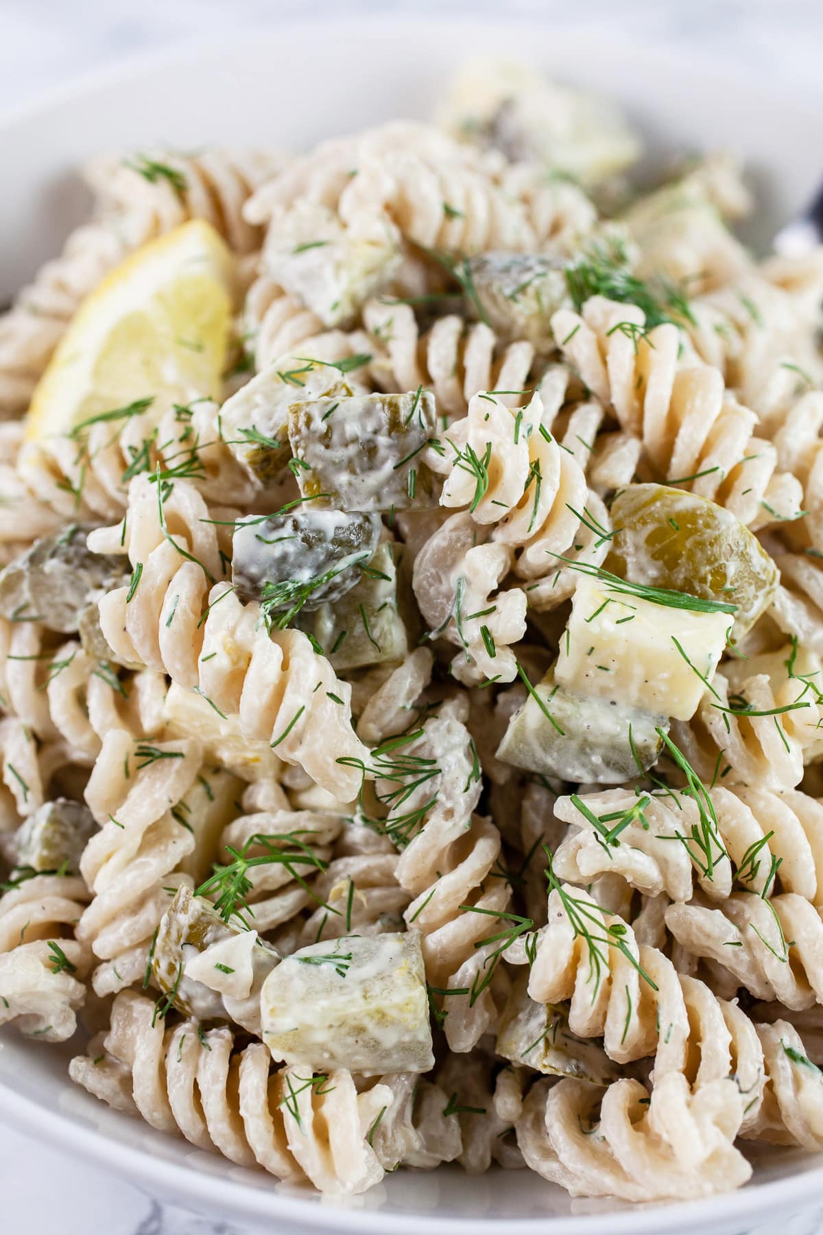 Dill pickle pasta salad in white bowl with lemon wedge.