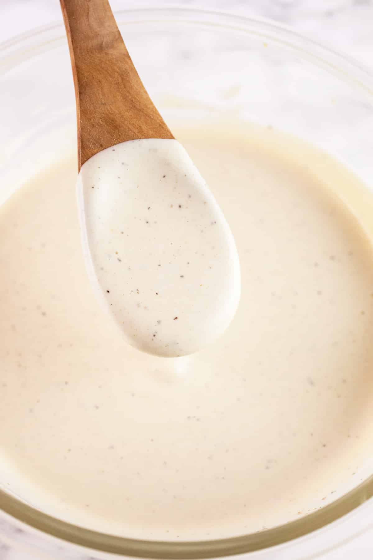 Creamy dressing on wooden spoon lifted from glass bowl.