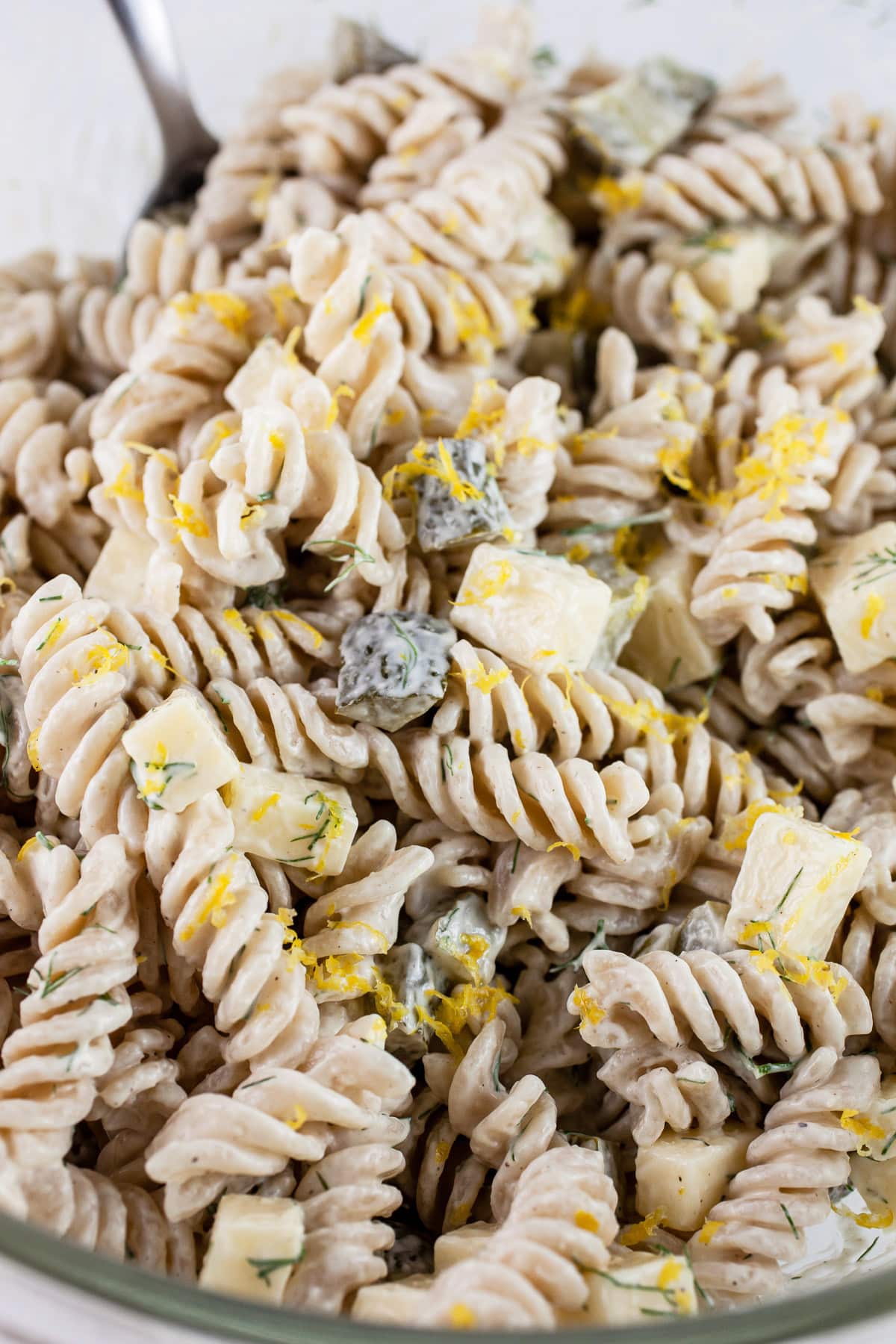 Dill pickle pasta salad with lemon zest in glass mixing bowl.