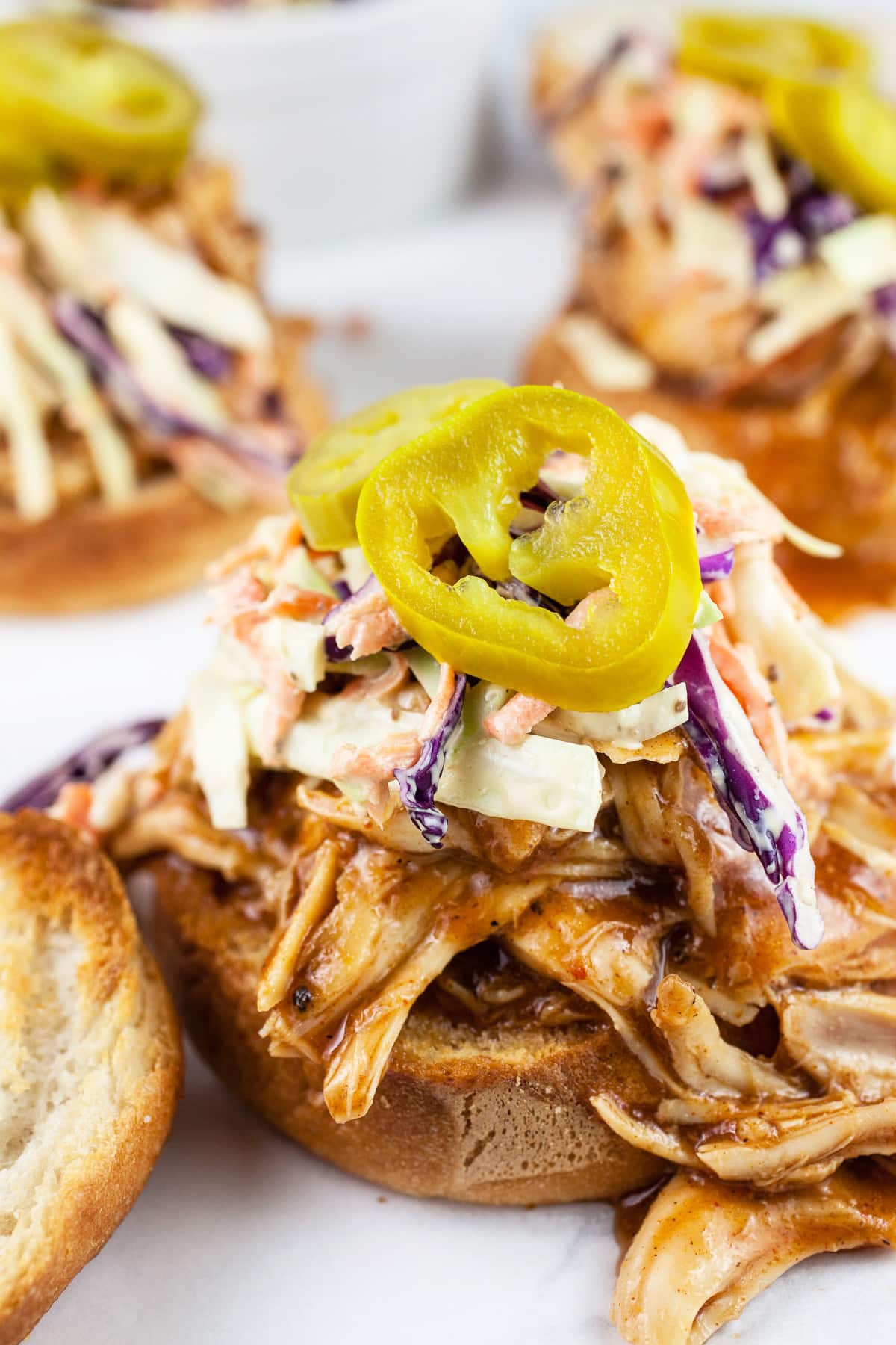 Open faced BBQ chicken sandwiches with coleslaw and pickled jalapenos on toasted buns.