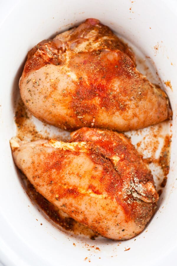 Uncooked split chicken breasts tossed in spices in slow cooker.