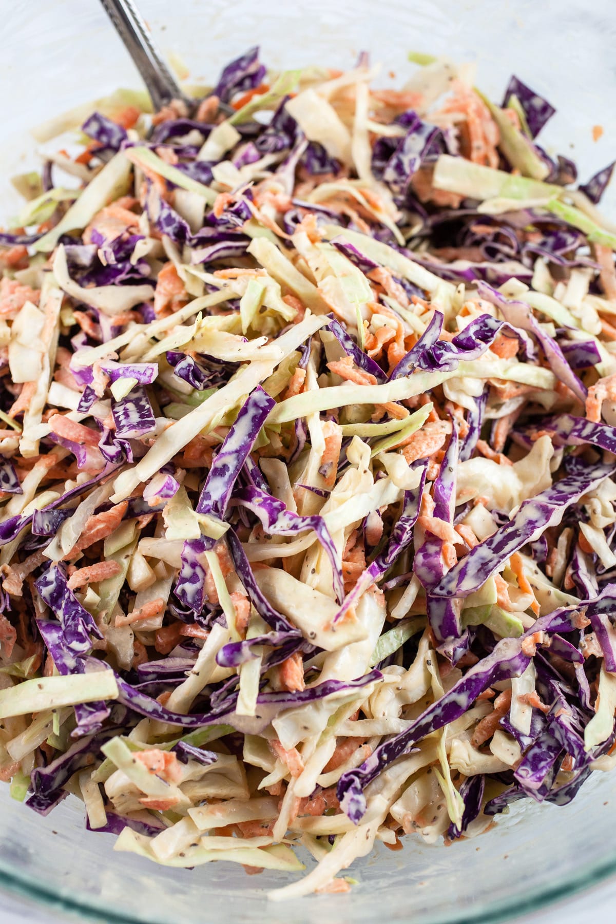 Shredded cabbage coleslaw in glass mixing bowl with spoon.