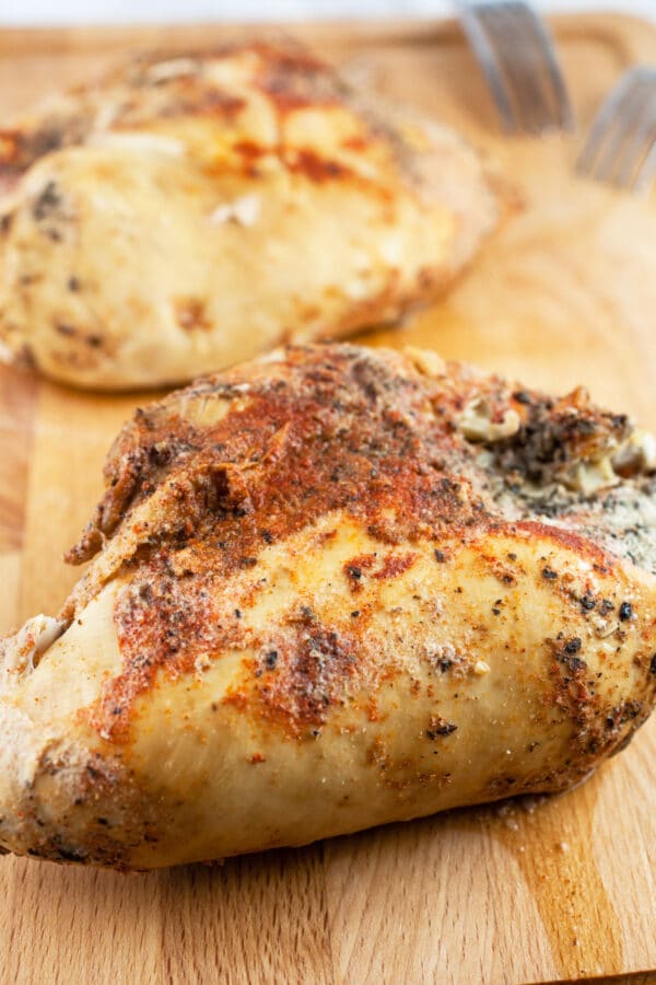 Cooked split chicken breasts on wooden cutting board.