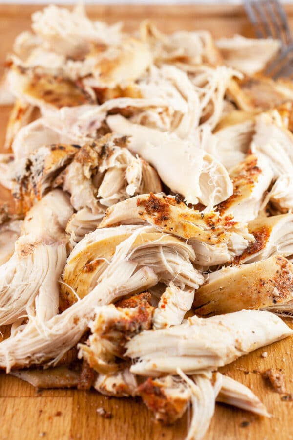 Cooked shredded chicken breasts on wooden cutting board.