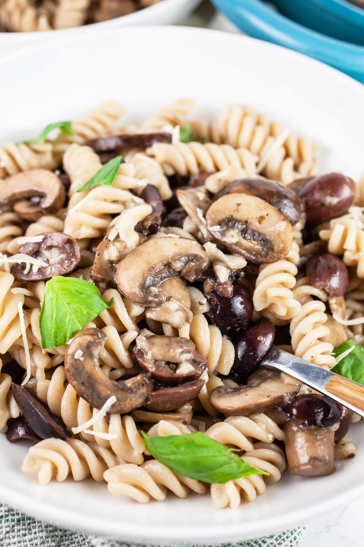 Mushroom olive pasta in white bowl with fork garnished with fresh basil.