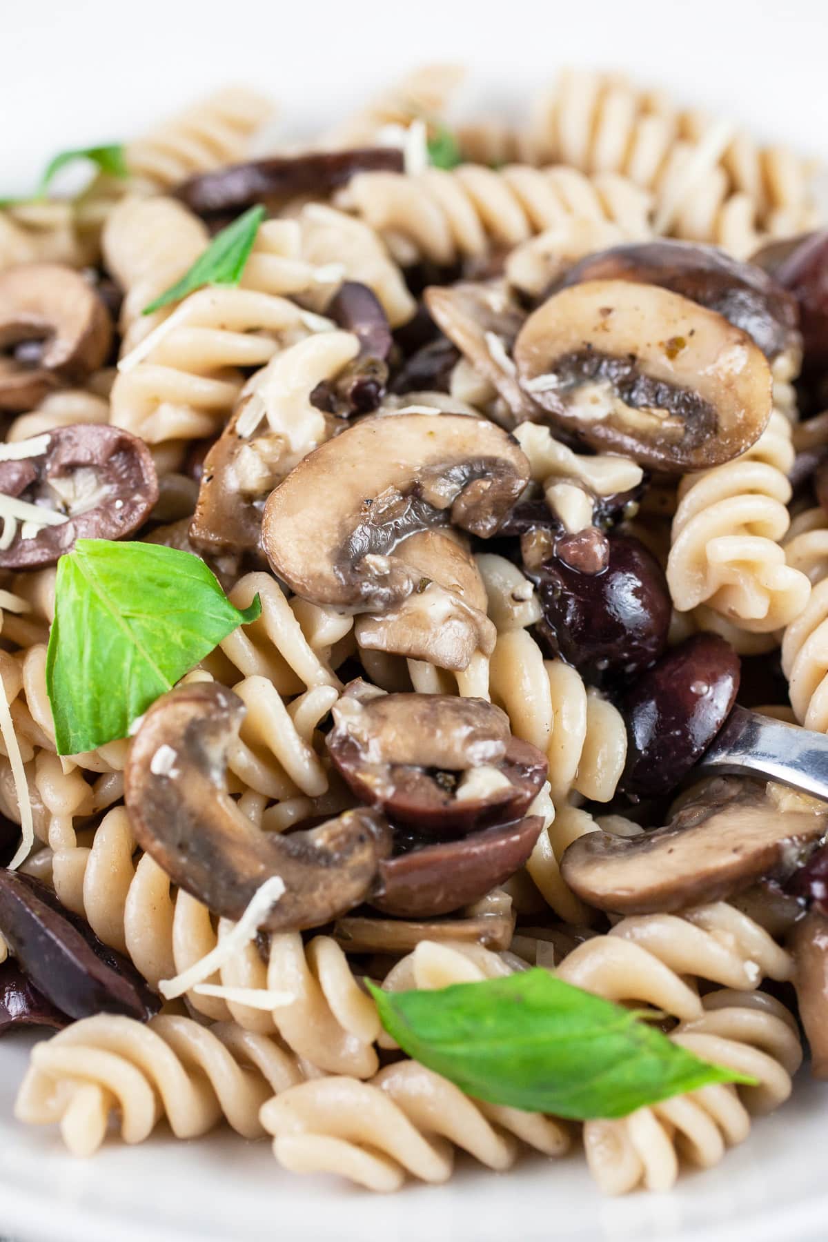 Mushroom olive pasta in white bowl with fork garnished with fresh basil leaves.