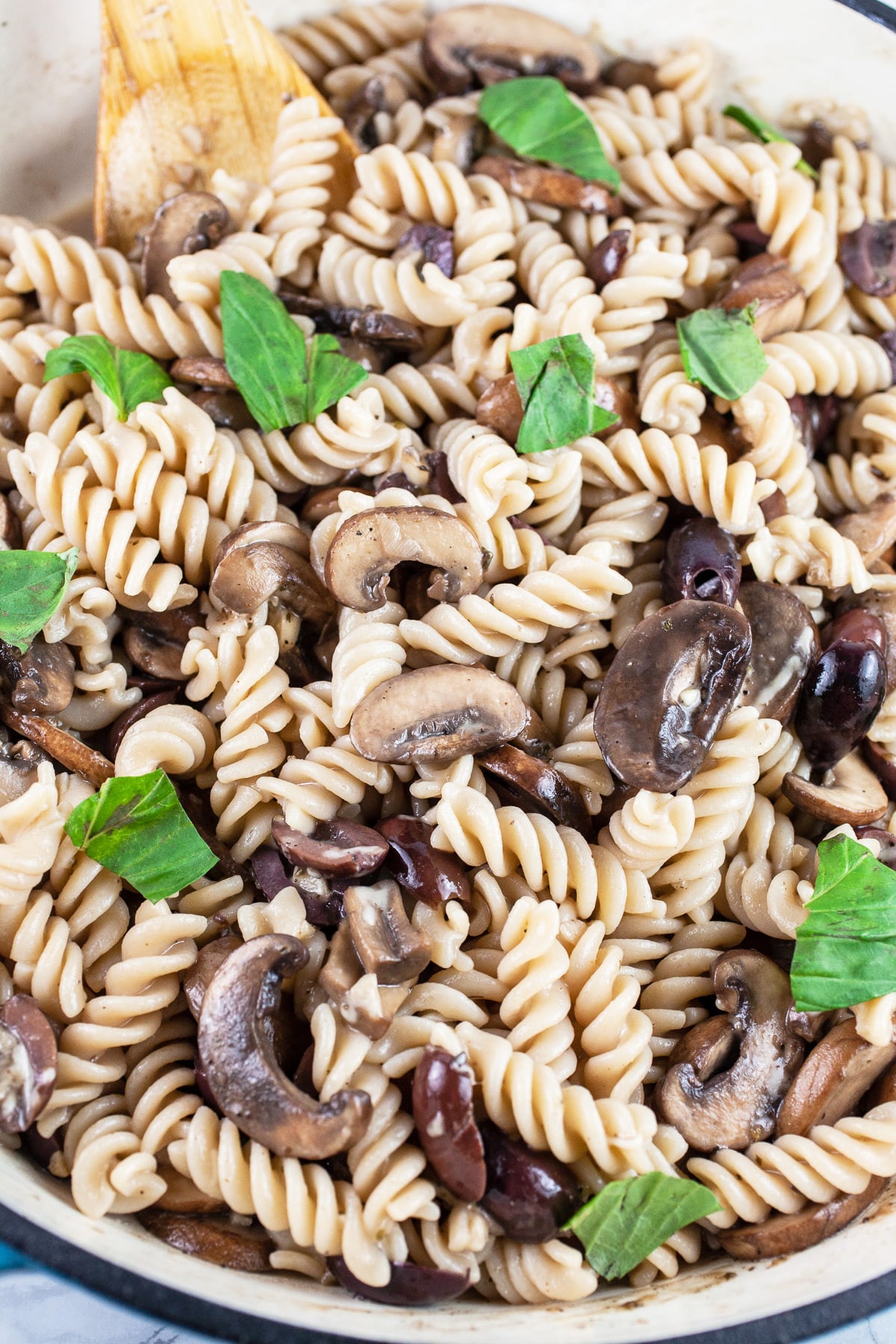 Olive mushroom pasta in skillet with freshly torn basil leaves.