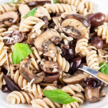 Mushroom olive pasta with fresh basil in white bowl with fork.