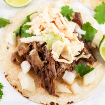 Slow cooker barbacoa beef tacos with slaw on corn tortillas.