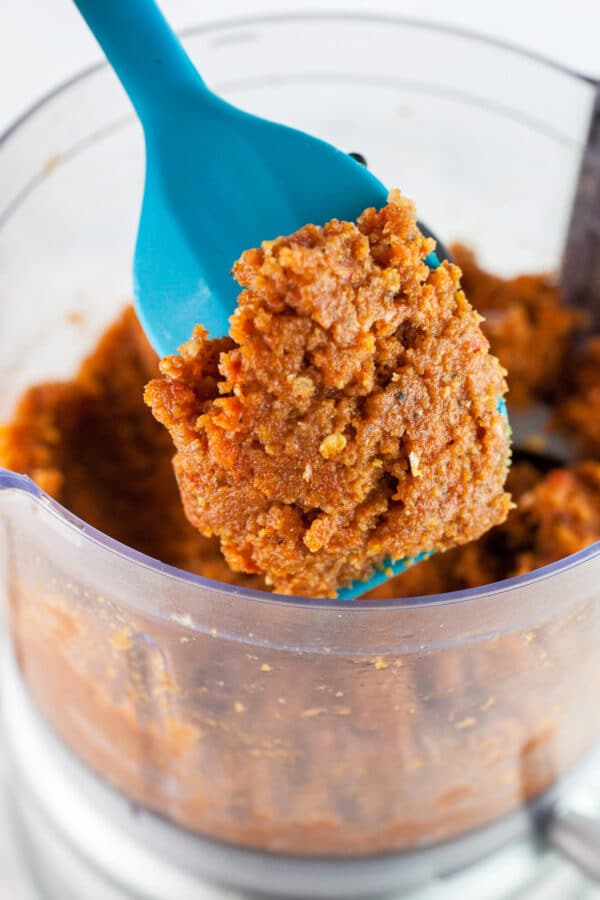 Scoop of sundried tomato pesto lifted from food processor on blue spatula.