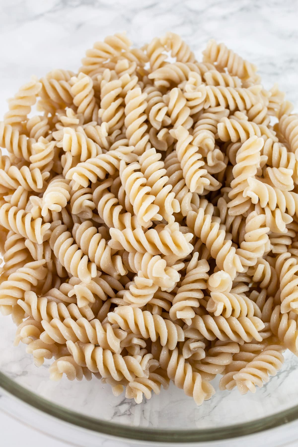 Cooked gluten free fusilli pasta in large glass mixing bowl.