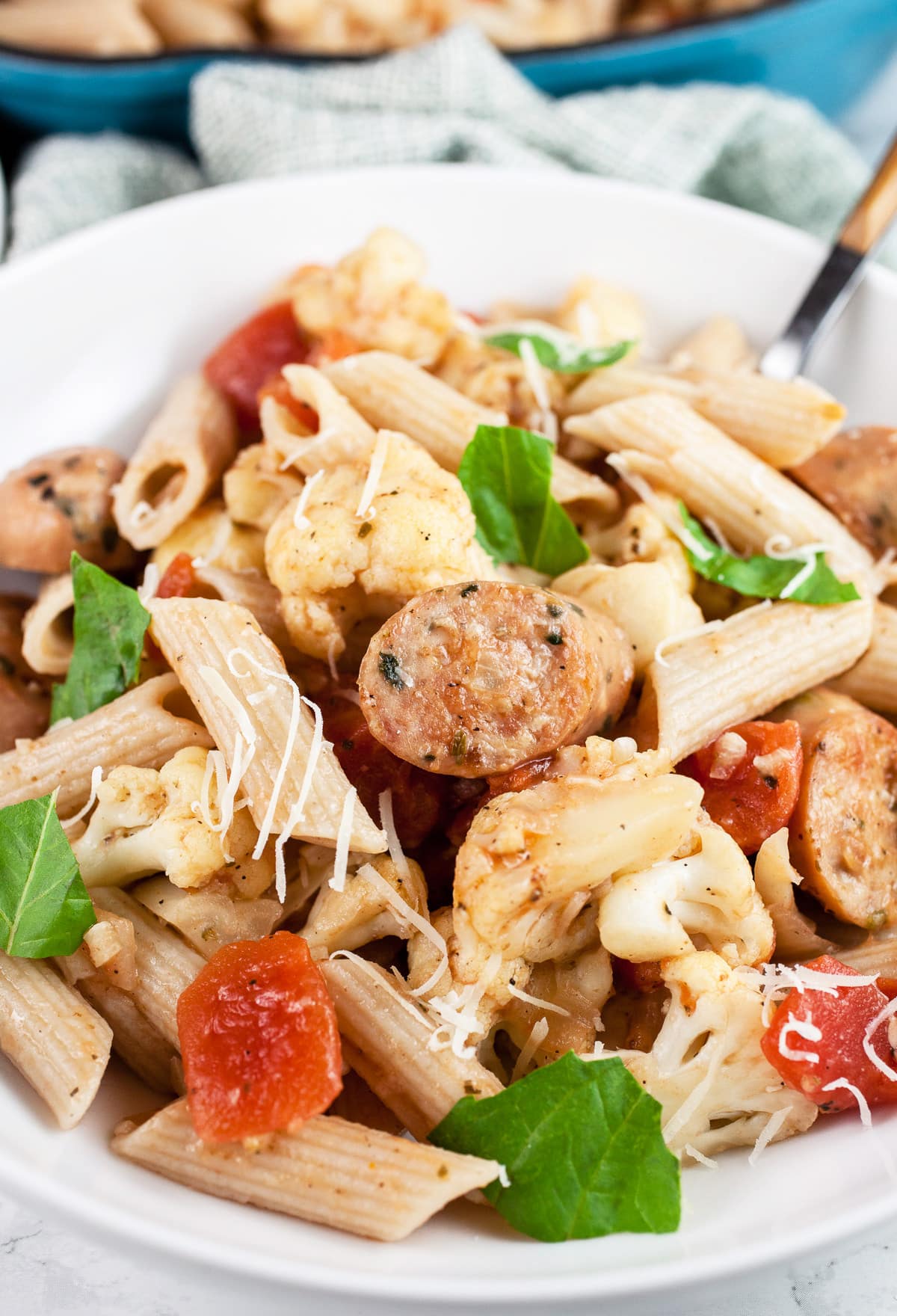 Cauliflower, tomato, and chicken sausage penne pasta in white bowl garnished with fresh basil.