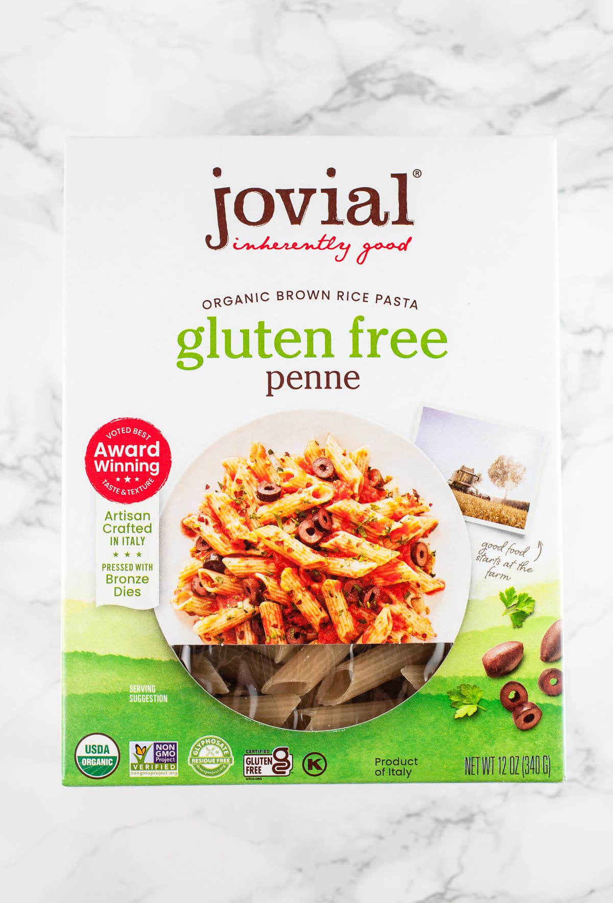Unopened box of Jovial penne pasta on white surface.
