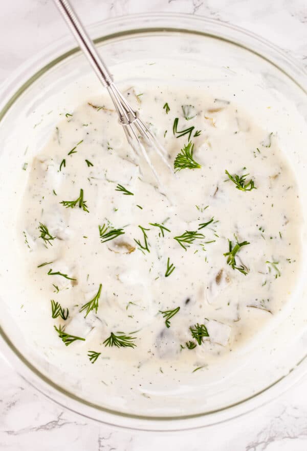 Tartar sauce with fresh dill in glass bowl with whisk.
