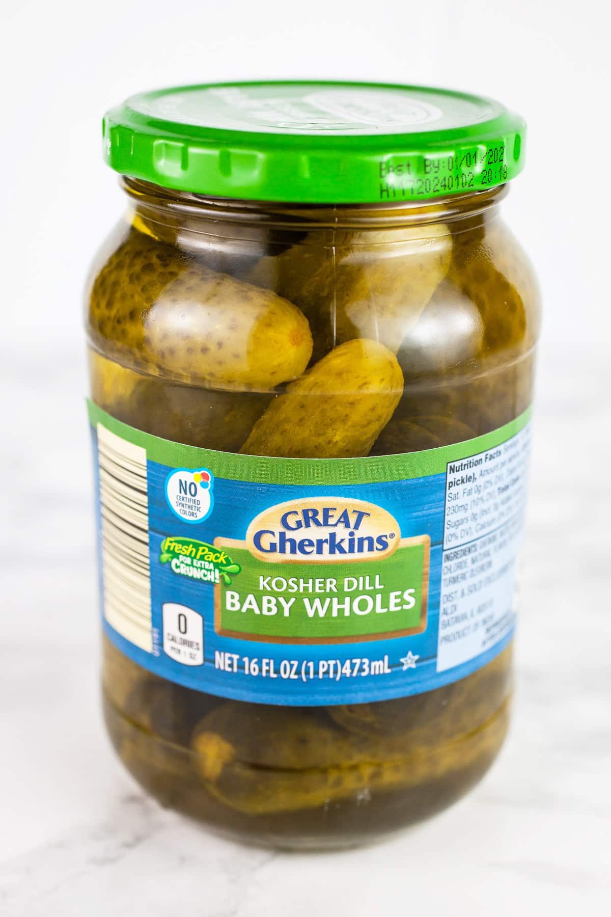Unopened jar of baby dill kosher pickles on white surface.