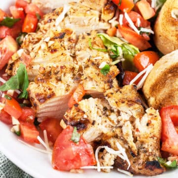 Grilled chicken breasts with bruschetta topping and toasted crostini in white bowl.