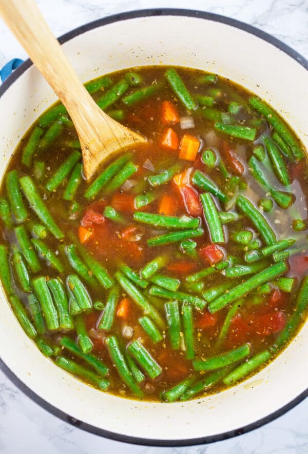 Green beans and carrots with vegetable broth in Dutch oven with wooden spoon.