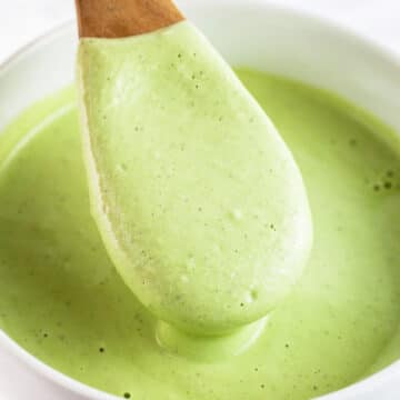 Cashew cilantro sauce lifted on wooden spoon from white bowl.