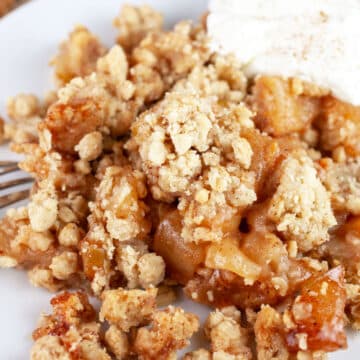 Gluten free apple crisp with whipped cream on white plate with fork.