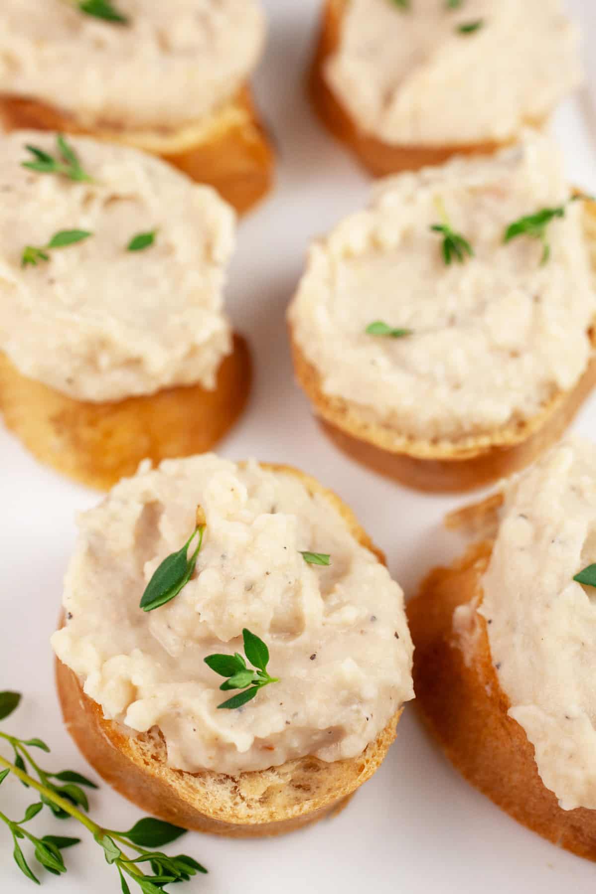 Crostini topped with white bean dip garnished with fresh thyme on white platter.