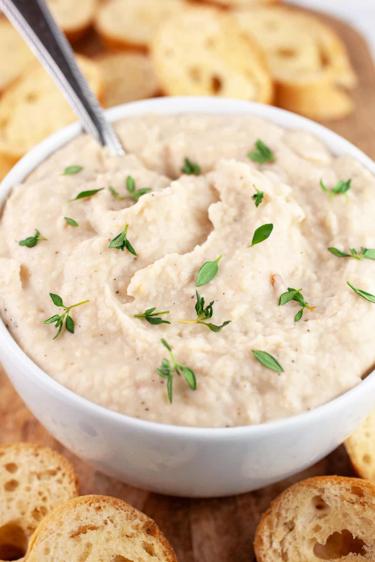 Italian white bean dip in white bowl on wooden platter with toasted crostini.